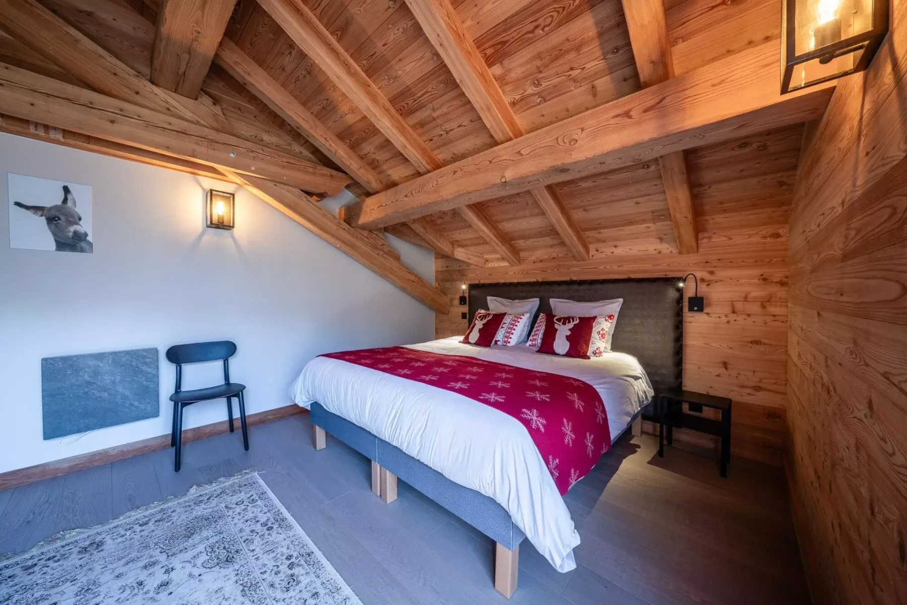 A bedroom with a bed dressed in white and red bedding beneath exposed wooden beams.