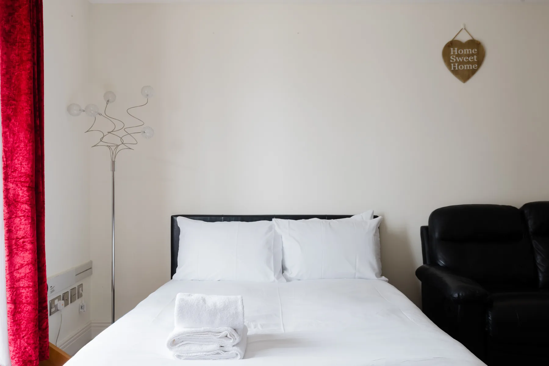 A bedroom with a neatly made bed and a black armchair.