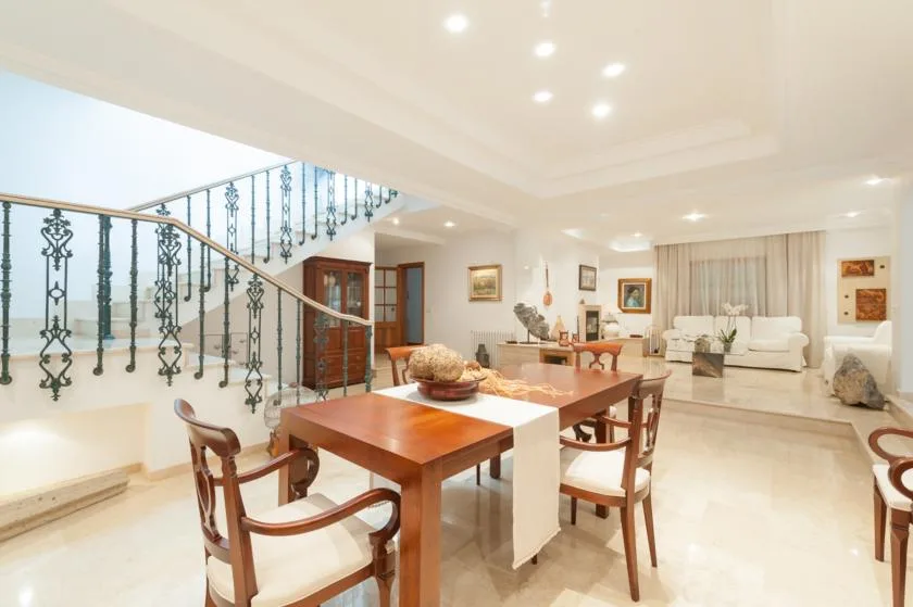 A bright dining area with a wooden table beside a staircase and living room.