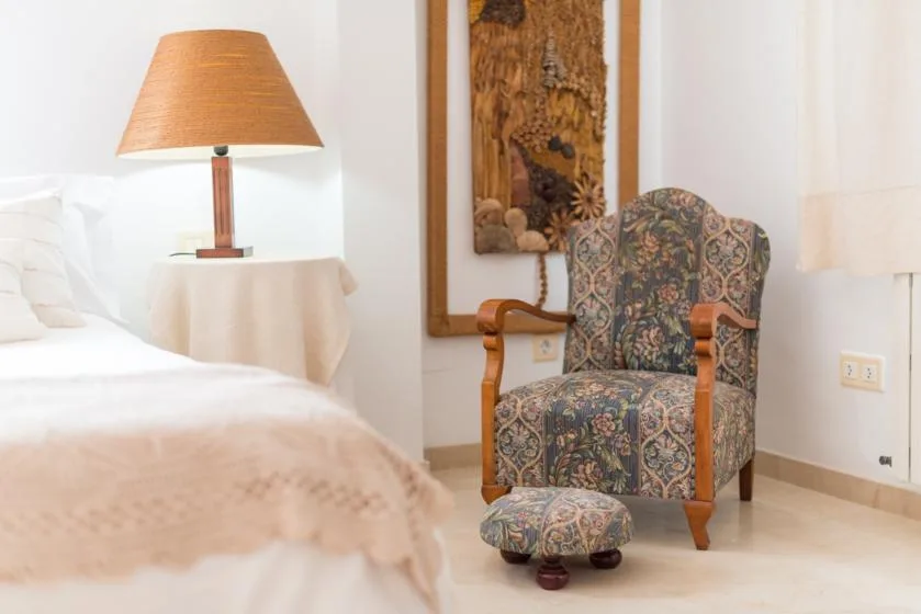 A bedroom seating area with a patterned armchair and a lamp beside the bed.