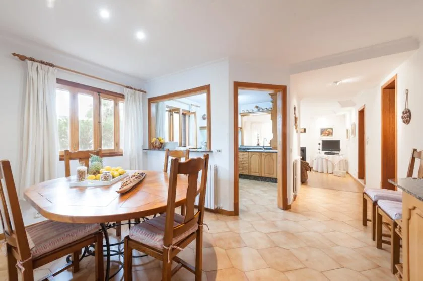 A dining area with a wooden table and chairs beside a bright hallway.