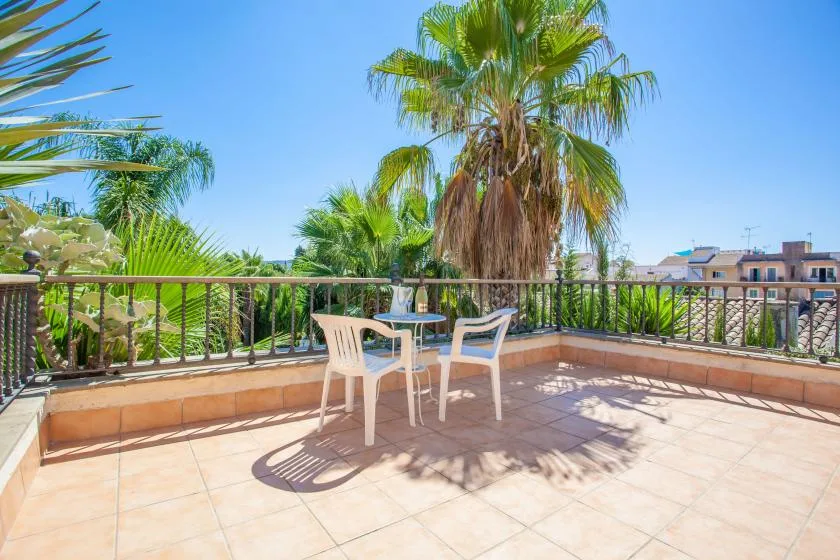 A tiled outdoor terrace has seating and a small table beside palm trees.