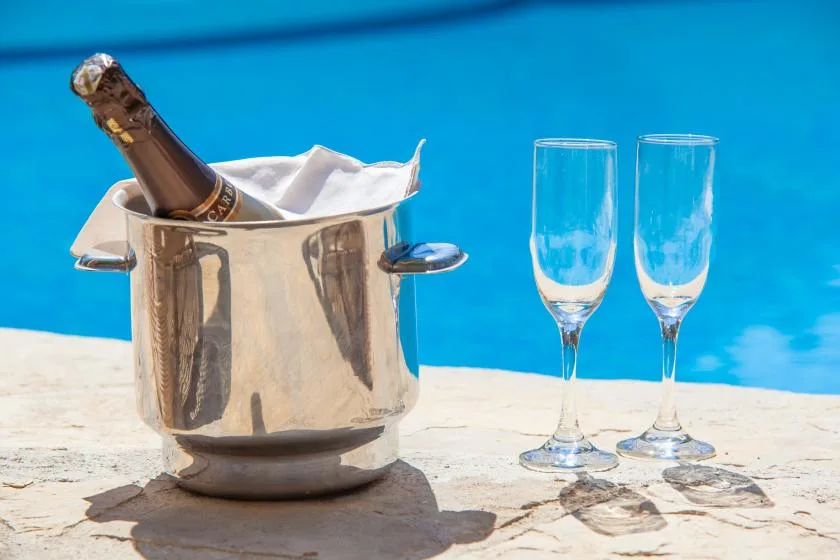 A champagne bucket and two glasses sit beside a swimming pool.