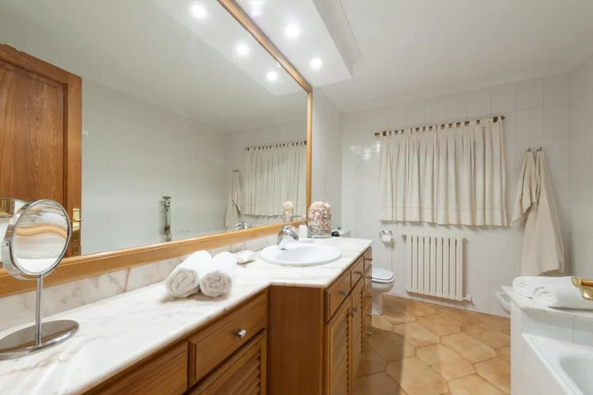 A bathroom with a long vanity, large mirror, and curtained window.