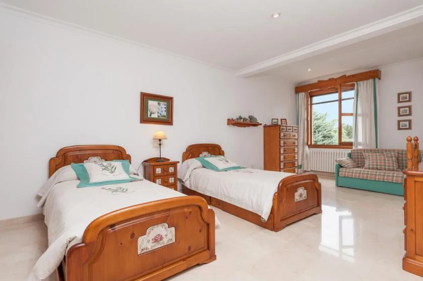 A bright bedroom with two wooden beds and a window overlooking greenery.