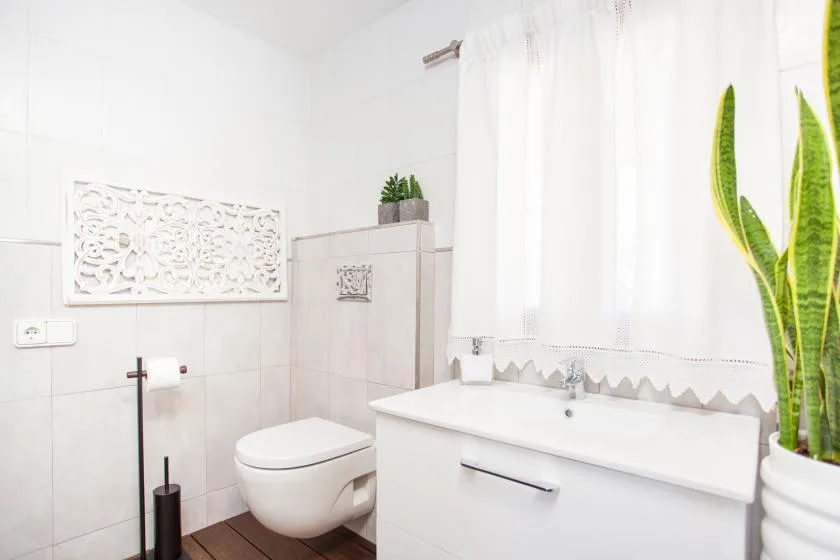 A bright bathroom with a bathtub, toilet, and white curtains.