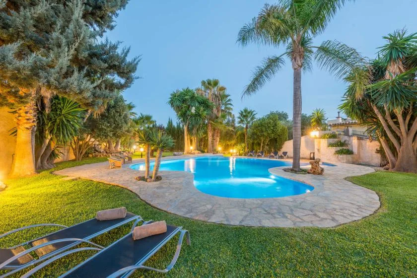 A swimming pool sits in a landscaped garden with palm trees and loungers.