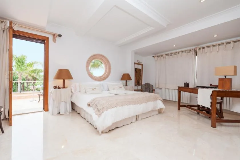 A bright bedroom with a large bed and an open doorway to a balcony.
