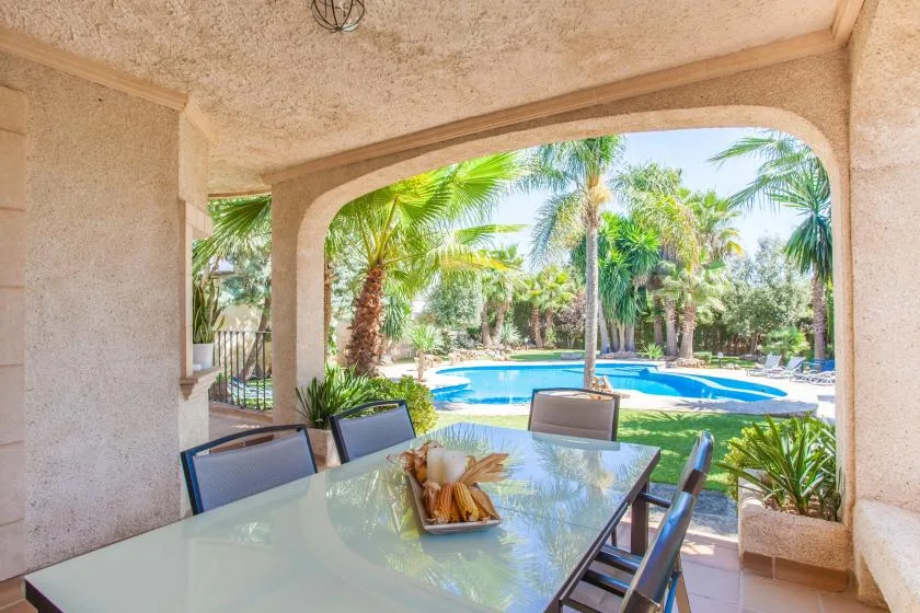 A covered patio dining area overlooks a swimming pool and palm trees.