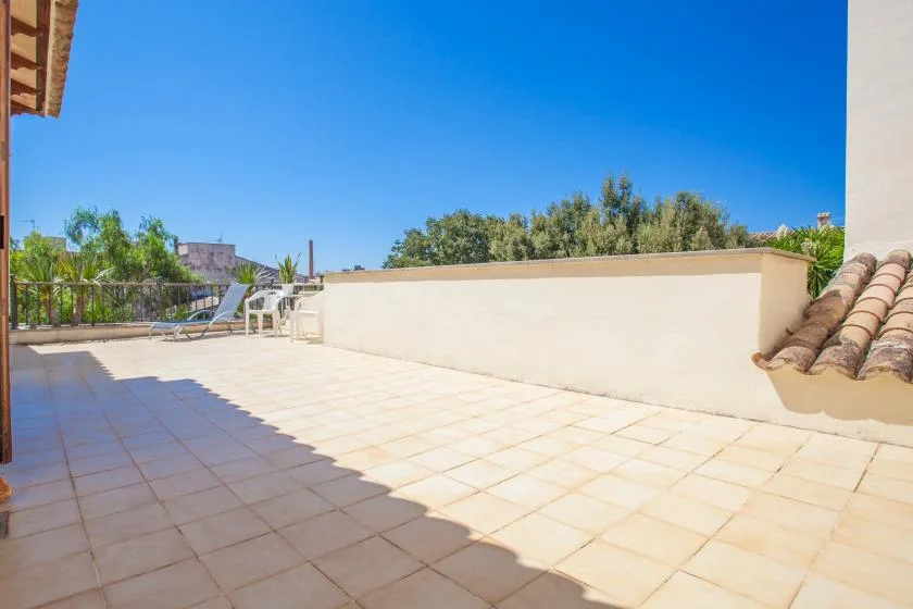 A sunny tiled terrace with a low wall and outdoor seating.