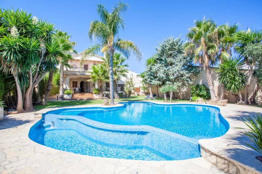 A swimming pool sits in a landscaped courtyard with palm trees and a building behind it.