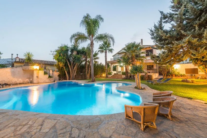 An outdoor swimming pool surrounded by palm trees, seating, and a landscaped garden.