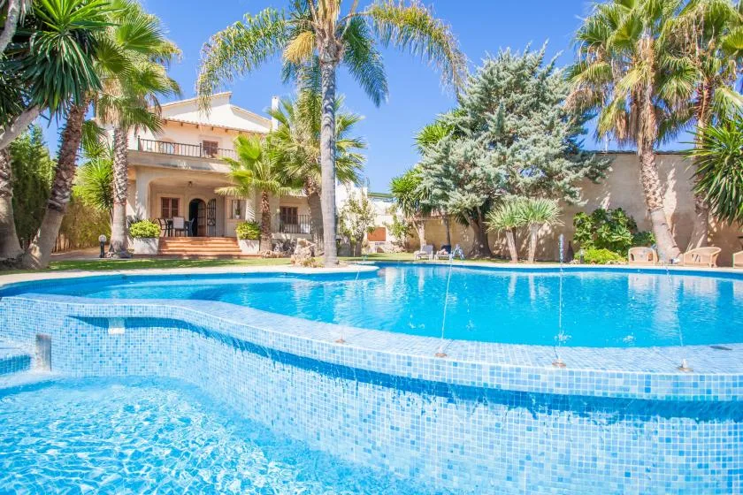 An outdoor swimming pool sits in front of a building surrounded by palm trees.
