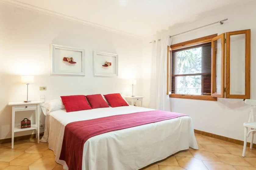 A bedroom with a bed dressed in white linens and red accents.