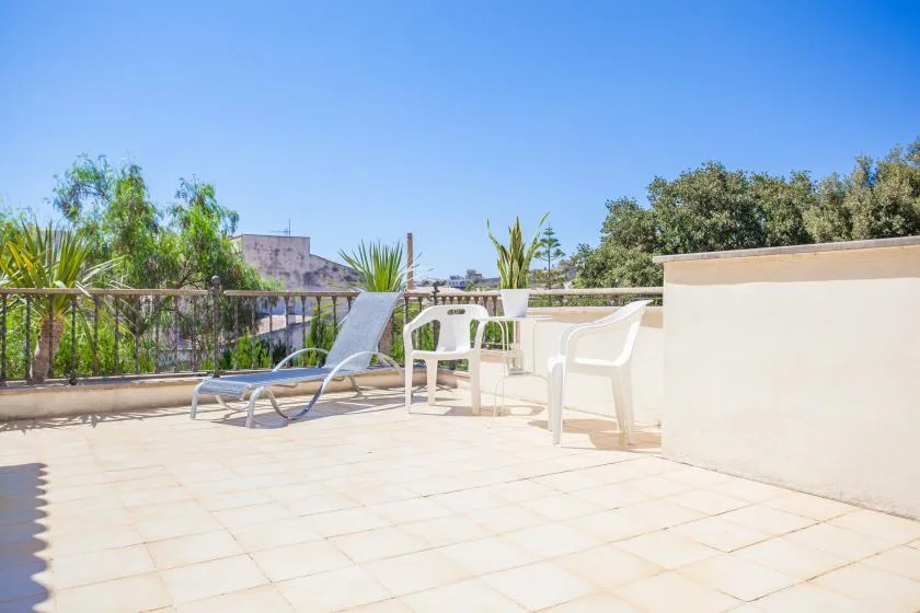 A sunny outdoor terrace with seating and leafy plants along the railing.