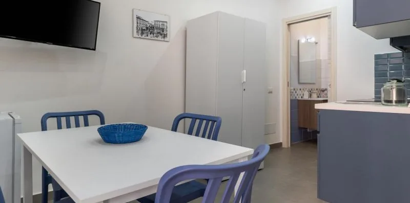 A dining area with a white table and blue seating beside a compact kitchen.