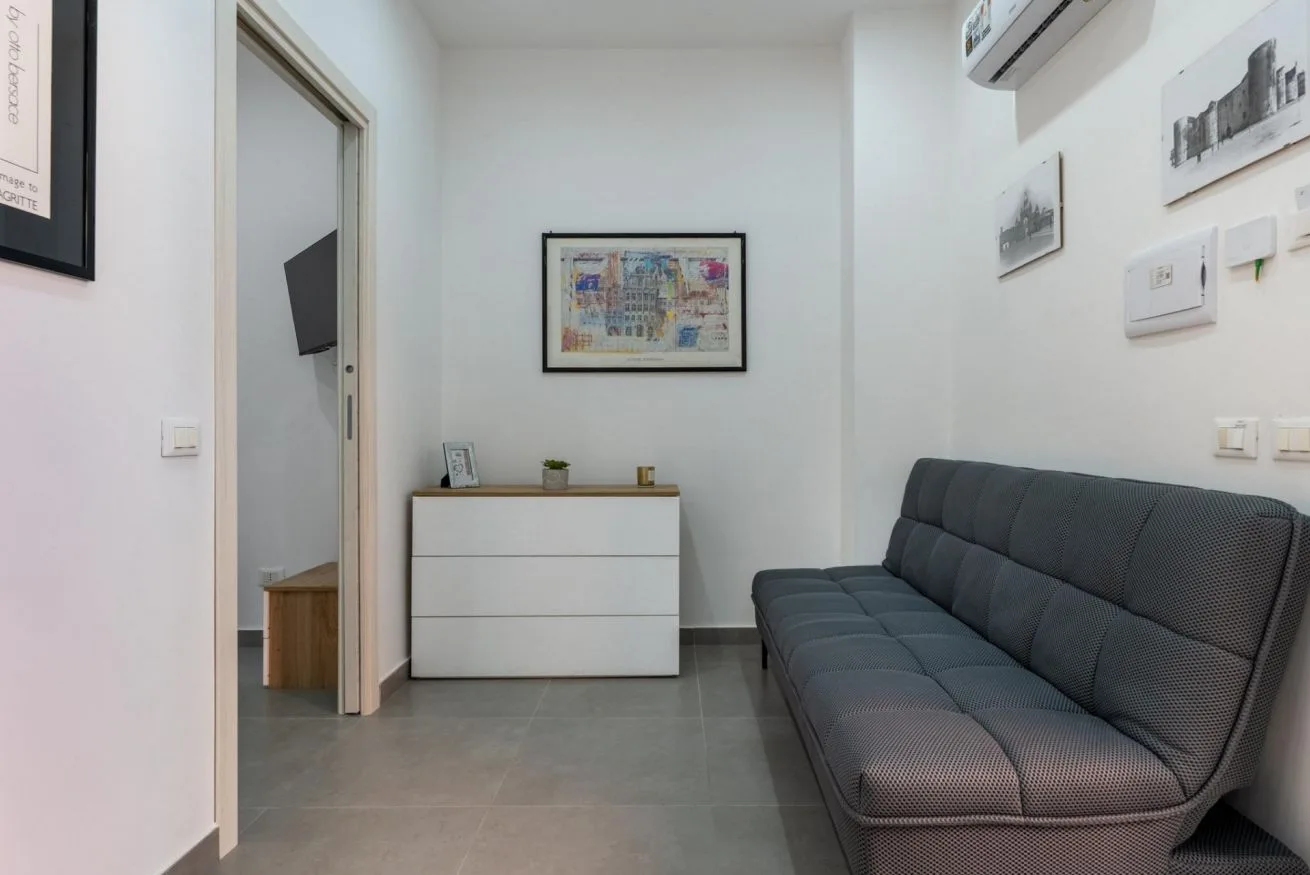 A narrow living area with a gray sofa and a white cabinet against the back wall.
