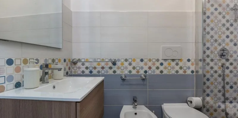 A tiled bathroom with a sink, toilet, and colorful patterned accents.