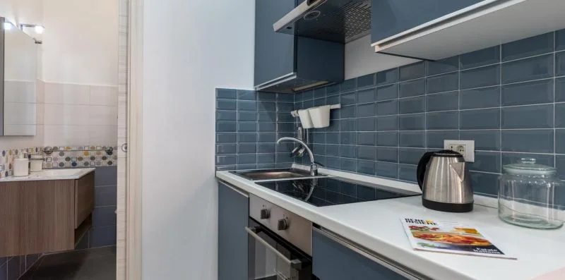 A compact kitchen with a dark tiled backsplash, cooktop, and kettle.