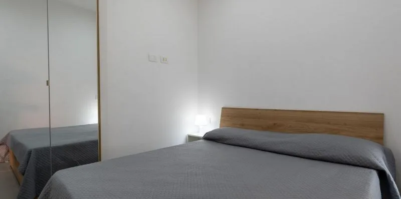 A bedroom with a bed covered by gray bedding and a wooden headboard.