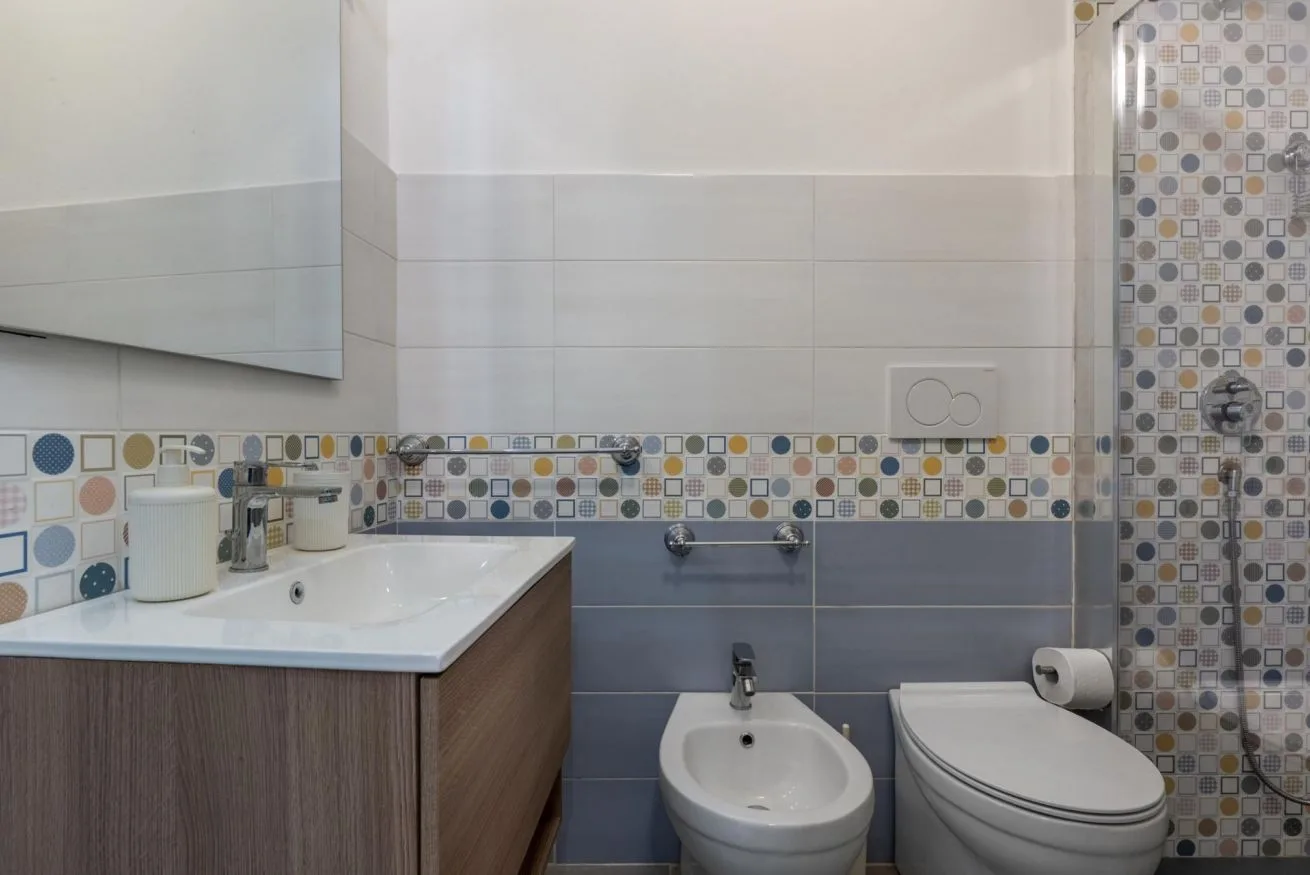 A tiled bathroom with a sink, bidet, toilet, and patterned shower area.