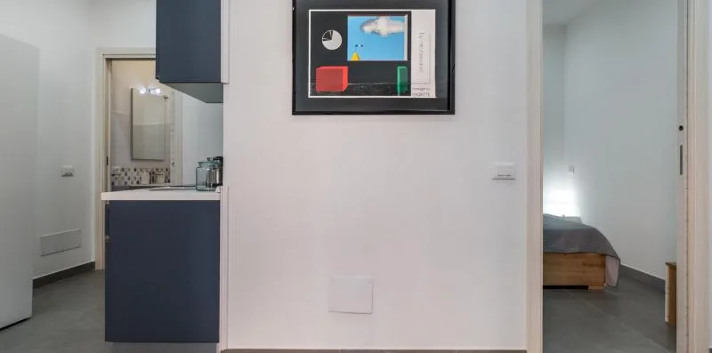 A white hallway connects a kitchenette with a bedroom doorway.