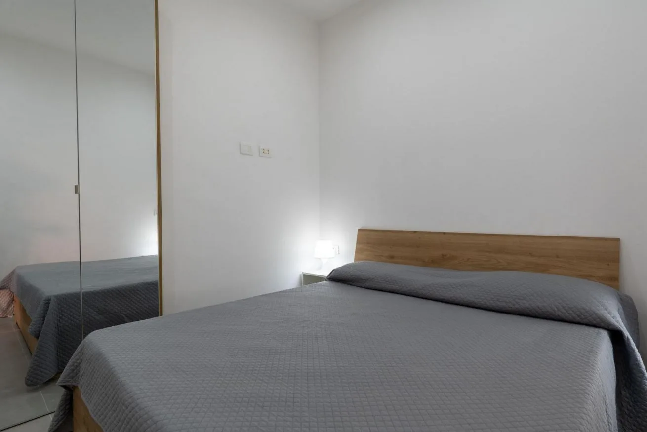 A bedroom with a neatly made bed and a mirrored wardrobe.