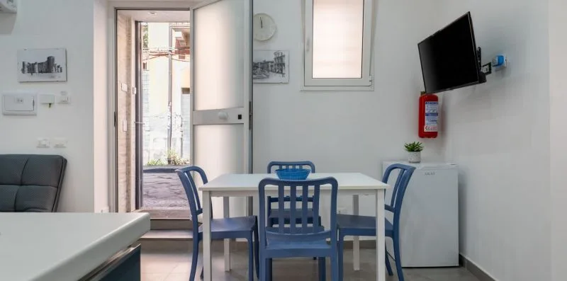 A dining area with a white table and blue seating beside an open doorway.