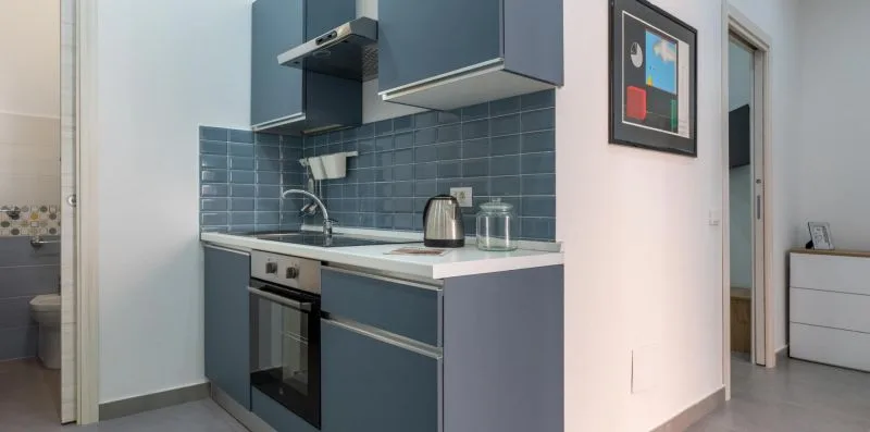 A compact kitchen with blue cabinets, a tiled backsplash, and countertop appliances.