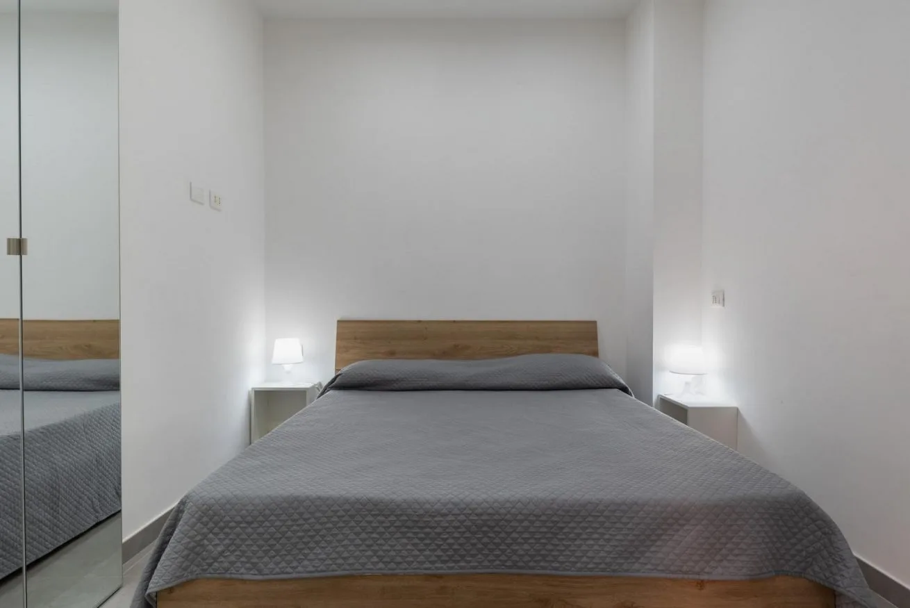 A bedroom with a bed covered in gray bedding and a mirrored wardrobe.