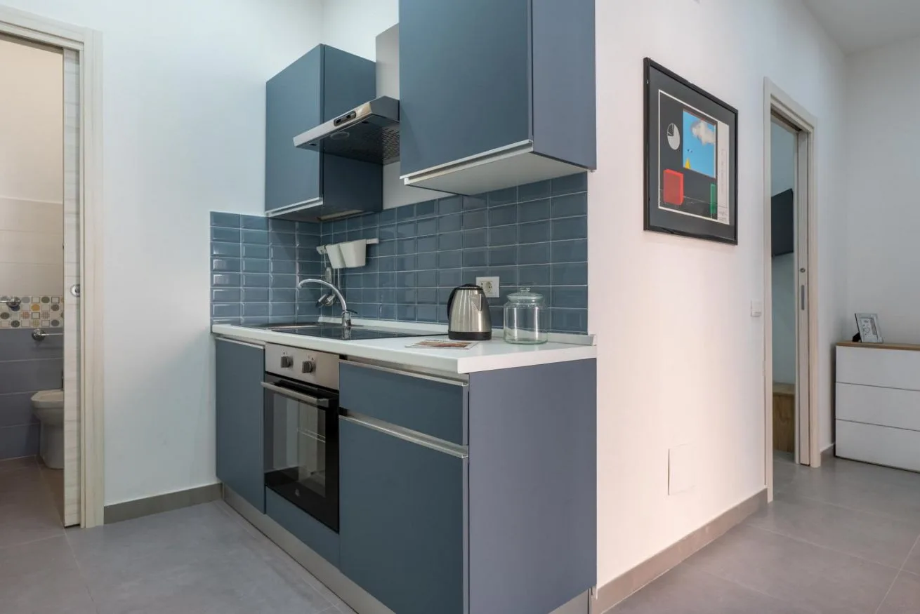 A compact kitchen with blue cabinets, a tiled backsplash, and a built-in oven.