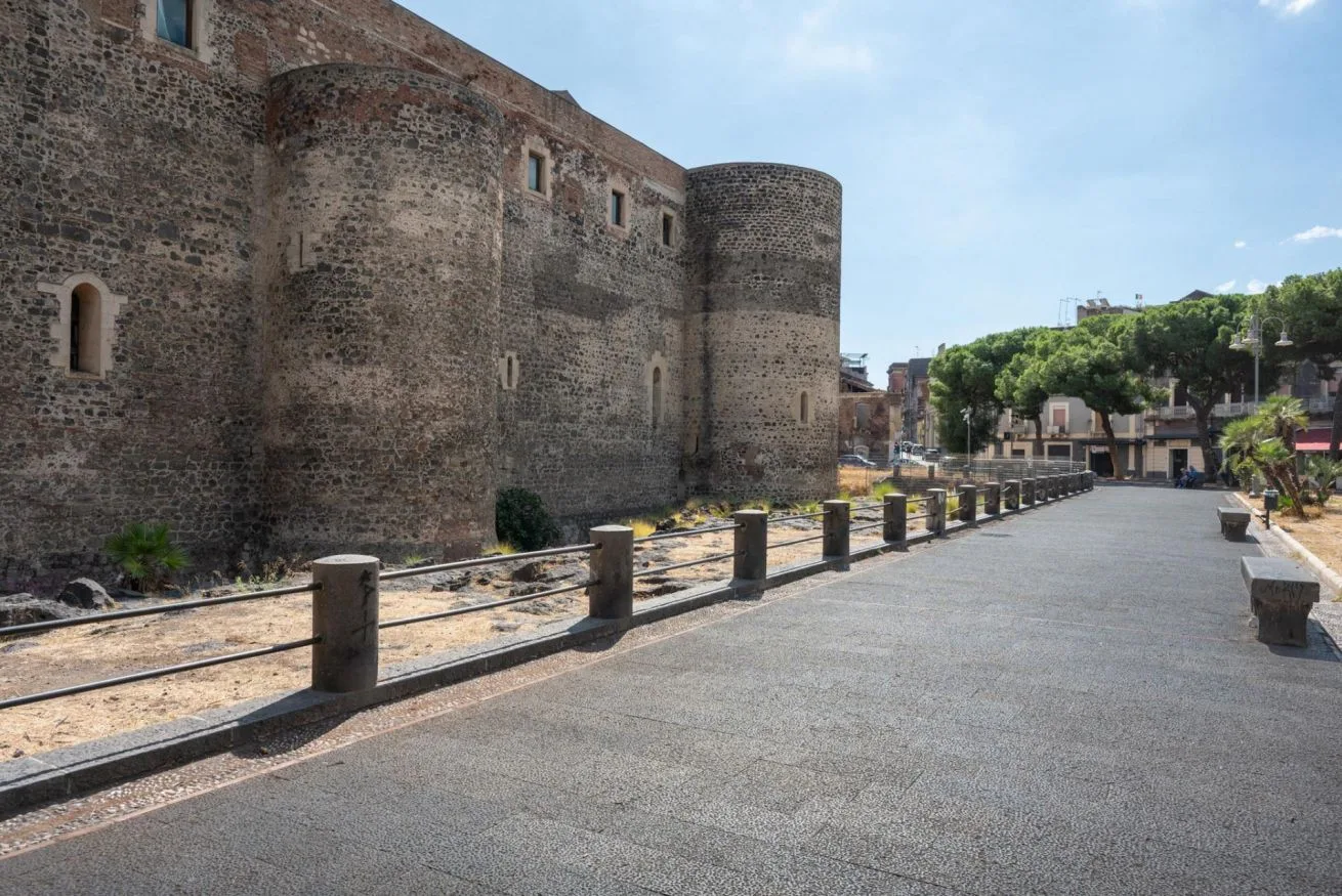 A paved walkway runs alongside a historic stone wall and round tower.