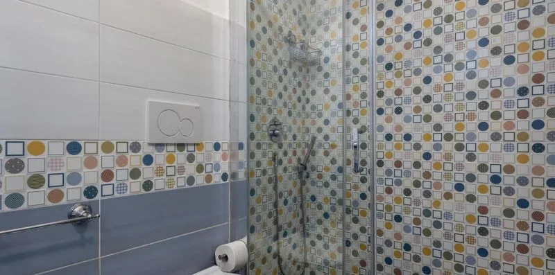 A tiled bathroom shower area with patterned walls and a glass shower screen.