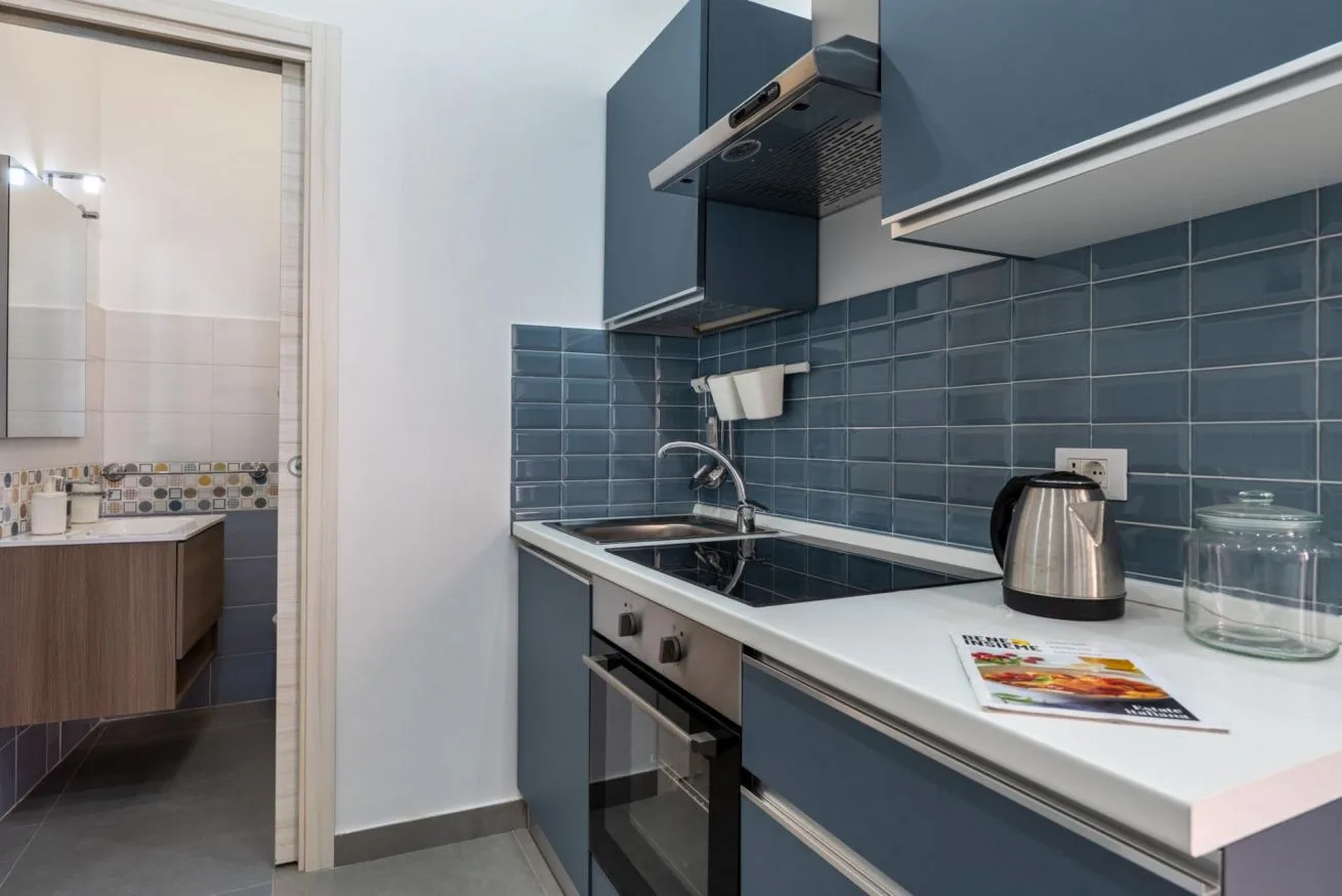 A compact kitchen with blue cabinets, a tiled backsplash, and a countertop.