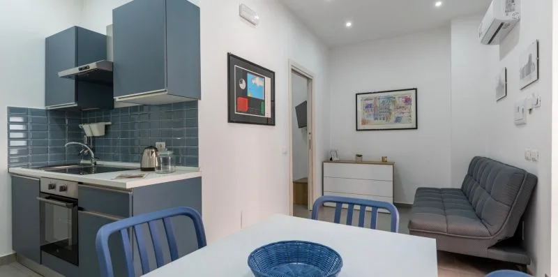 A compact kitchen and living area with blue cabinets, a table, and seating.
