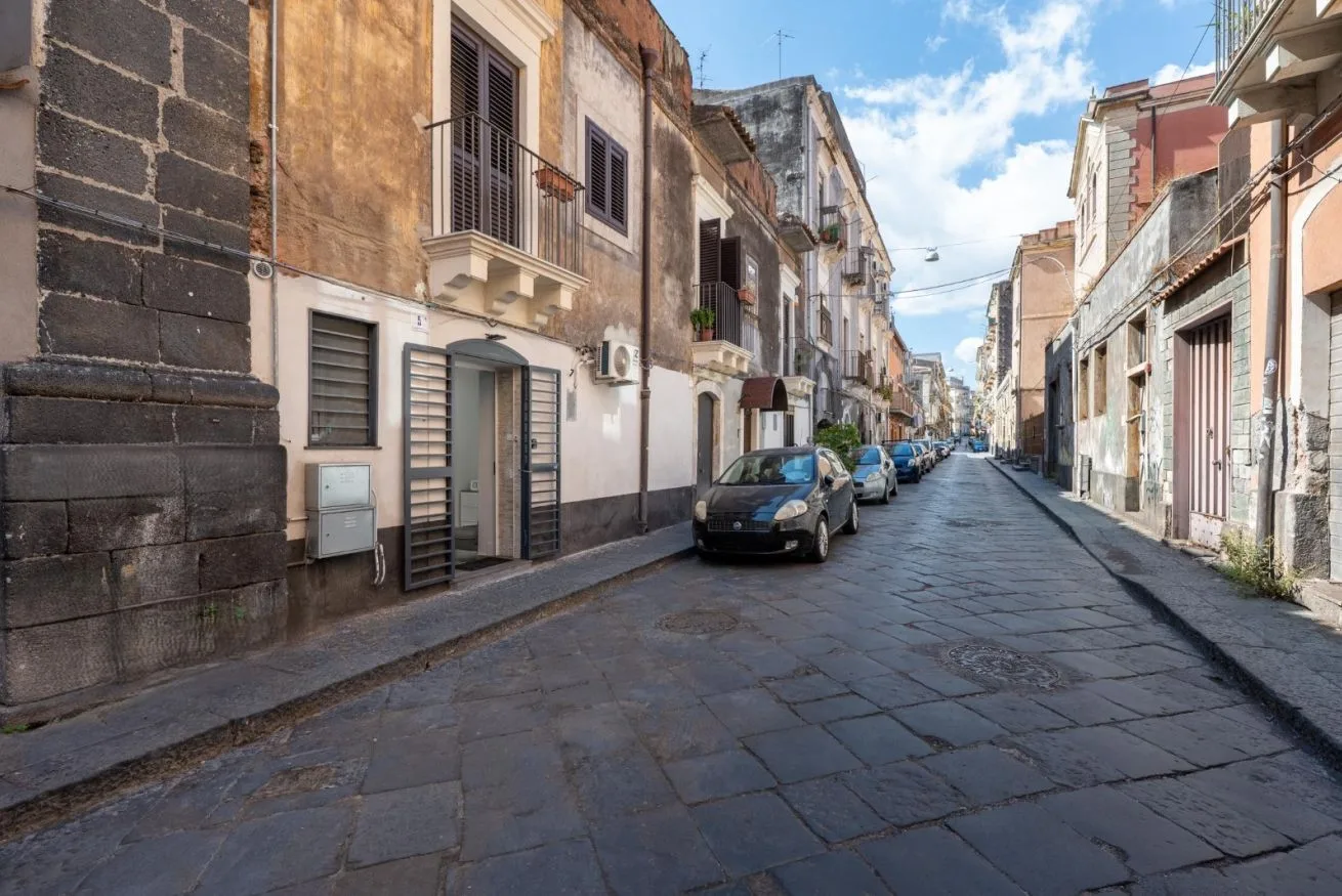 A narrow paved street lined with closely spaced buildings and parked cars.