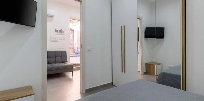 A bedroom with a bed, a wardrobe, and a doorway opening onto a sitting area.