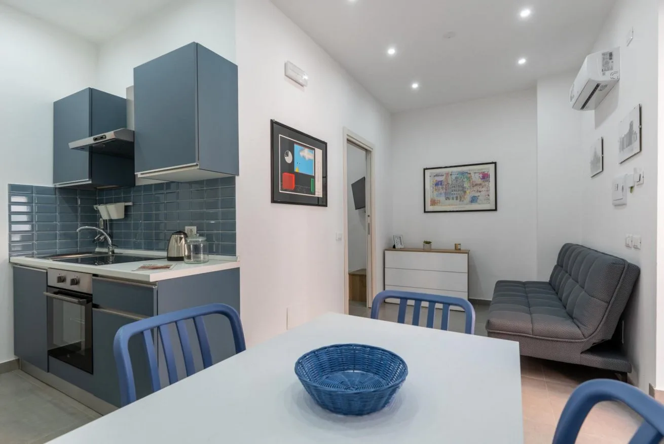 A compact kitchen and dining area with a table in the foreground and seating along the wall.