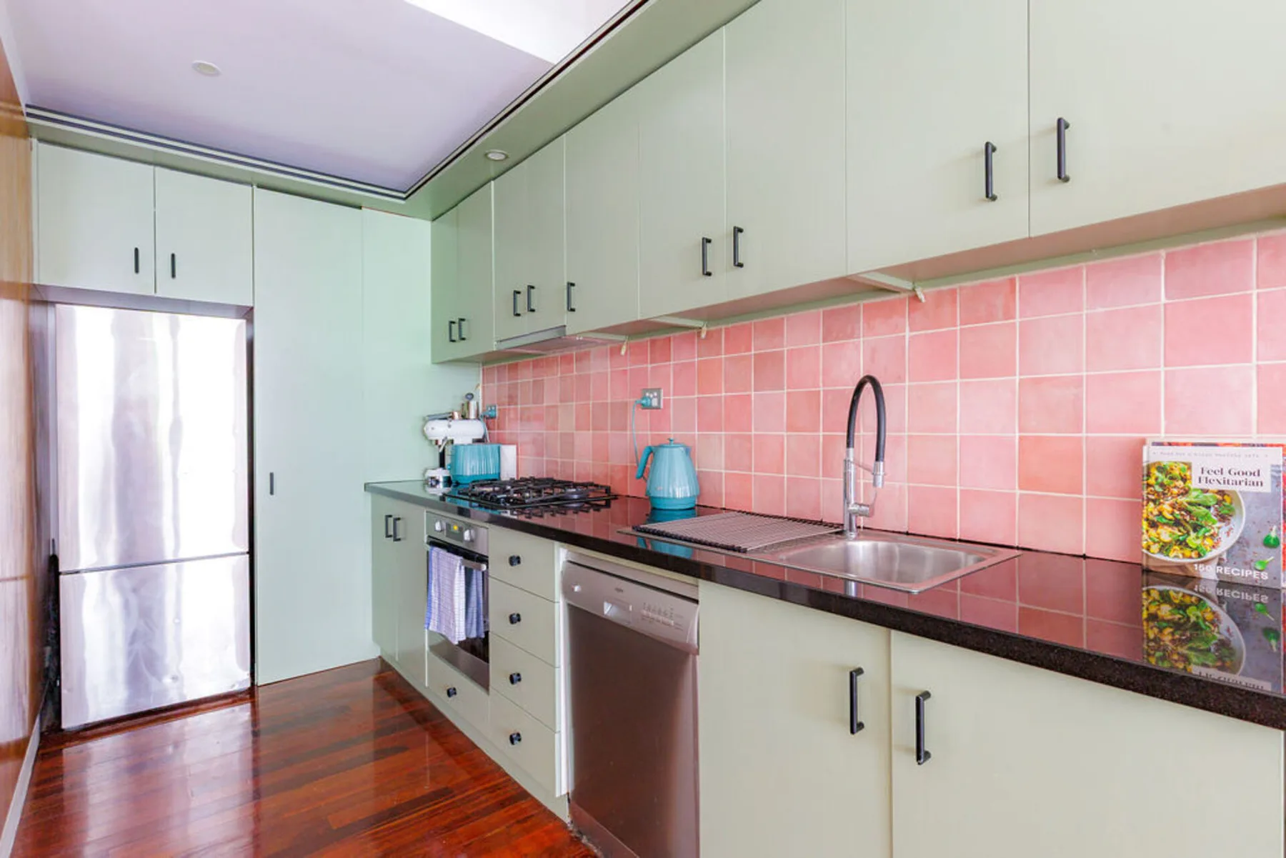 A kitchen with pale cabinets, a pink tiled backsplash, and a long counter.