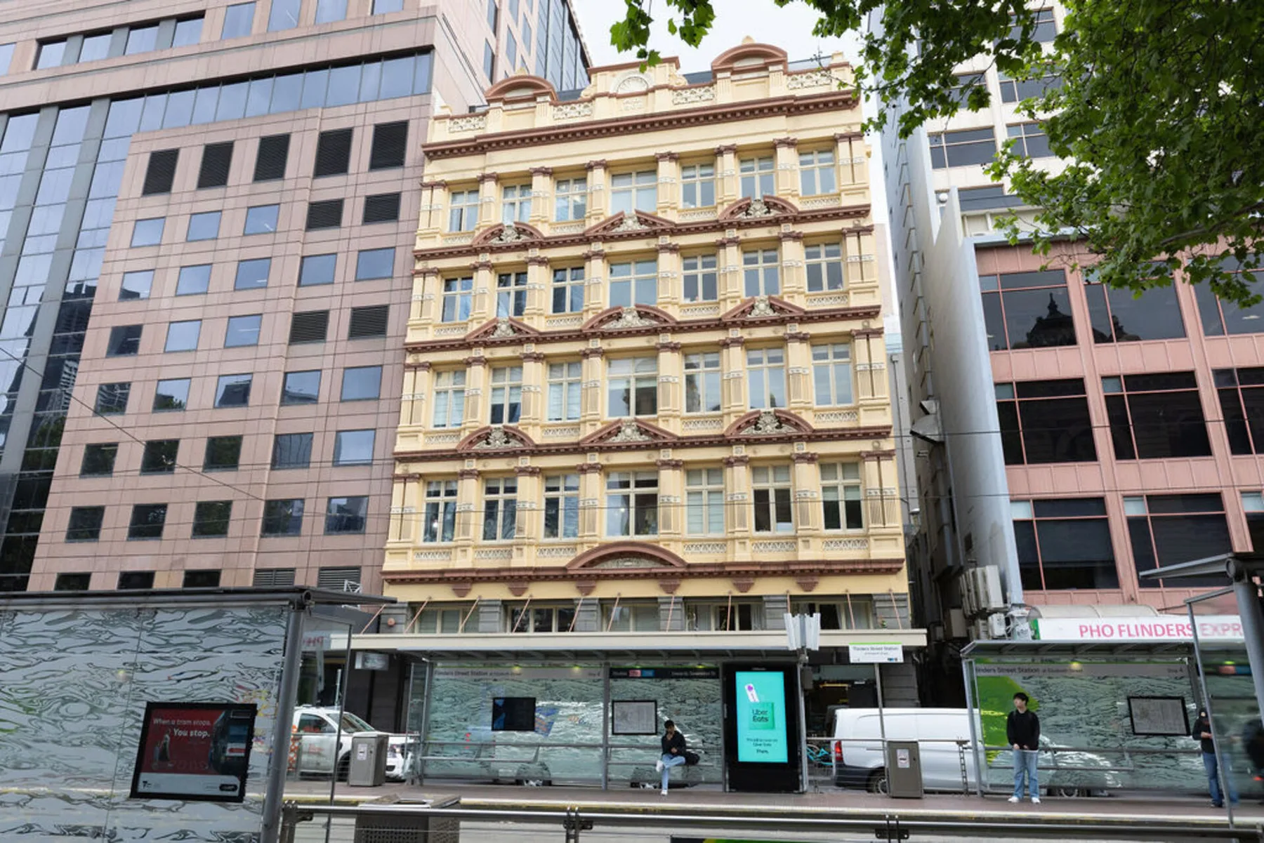 An ornate historic-looking building stands between modern office buildings on a city street.