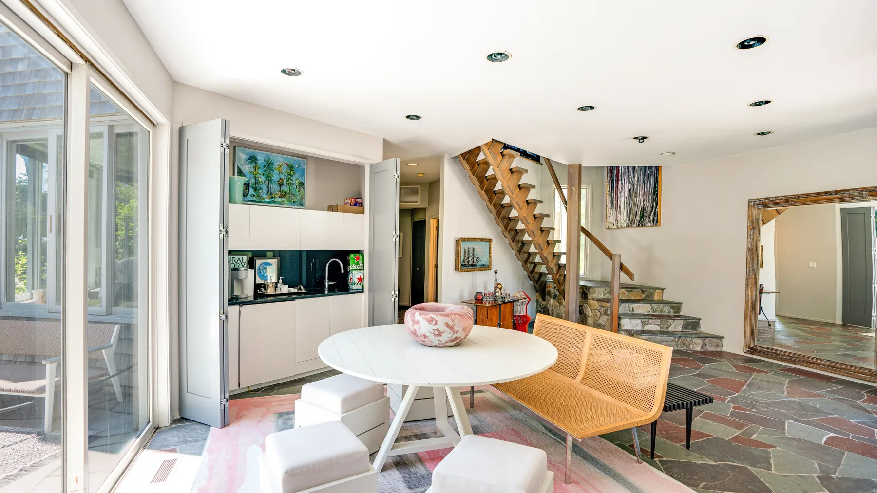 A bright dining area with a round table beside a staircase and large windows.