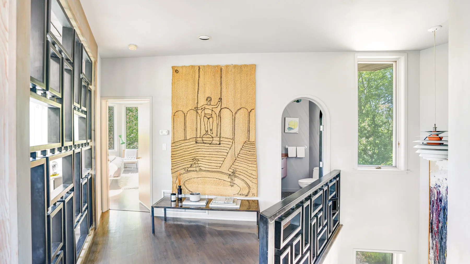 A bright interior hallway features a large tapestry and a dark railing.
