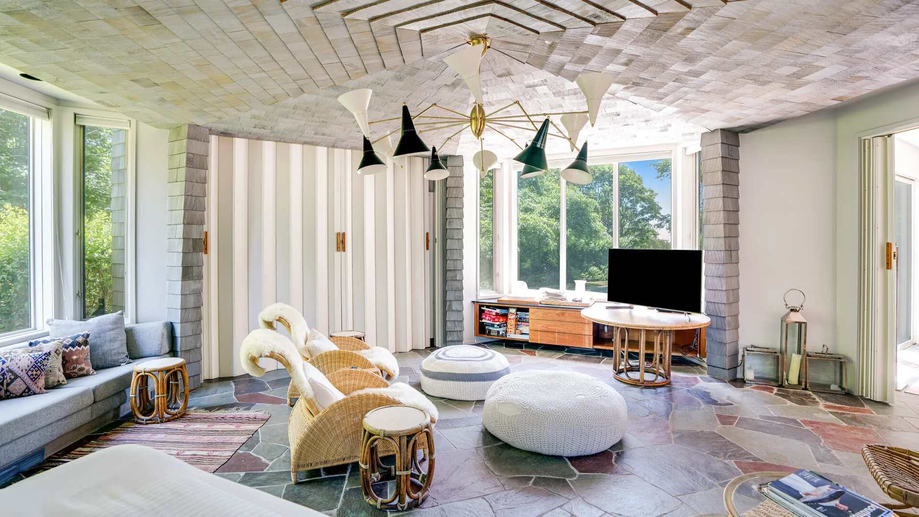 A bright living room with cushioned seating, a round ottoman, and large windows.