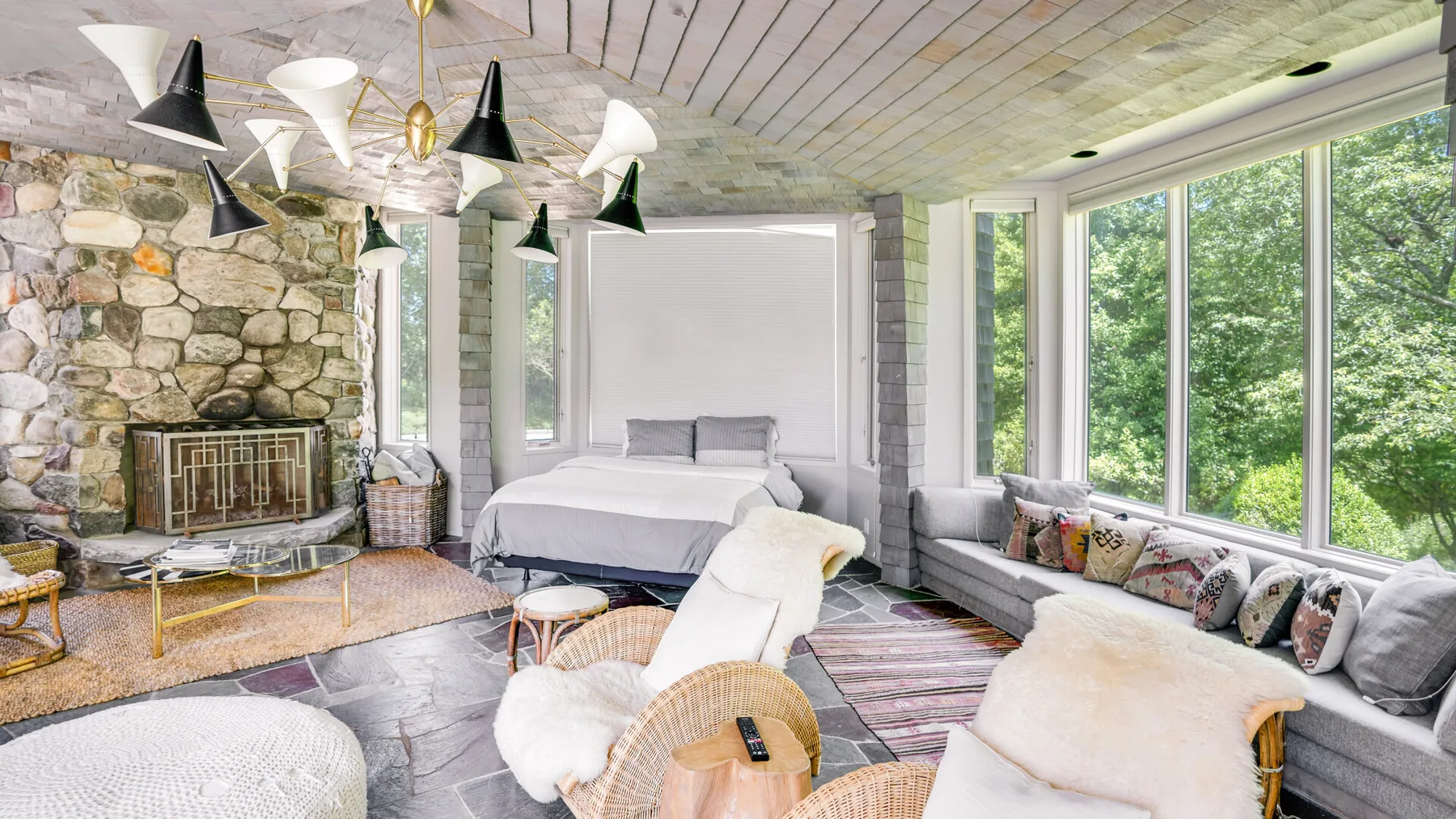 A bright bedroom with a bed, seating, and large windows overlooking greenery.