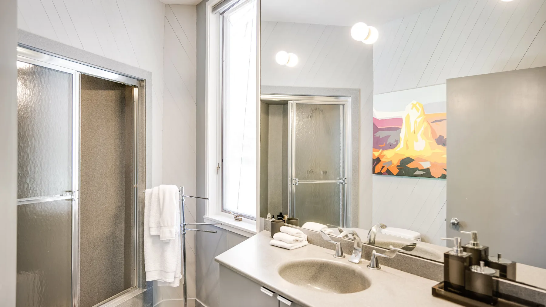 A bright bathroom with a wide vanity, mirror, and shower.