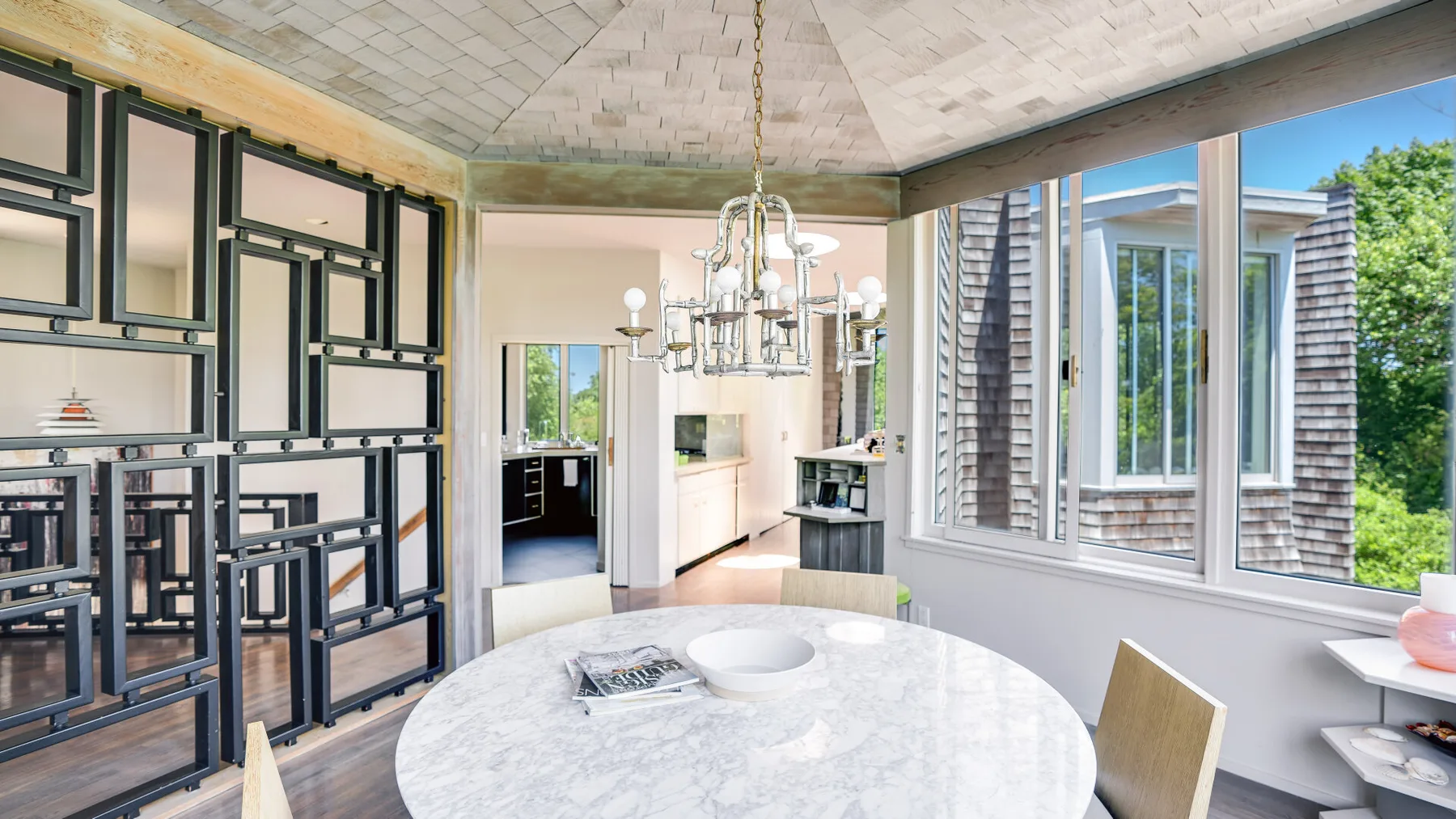 A bright dining area with a round table, chandelier, and large windows.