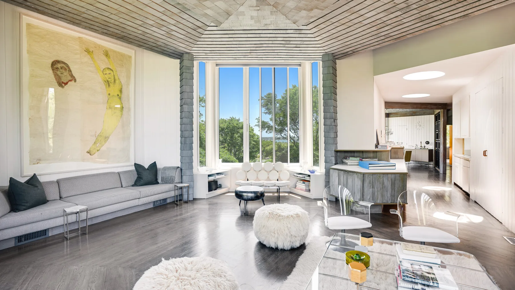 A bright living room with a large window and seating around a low table.