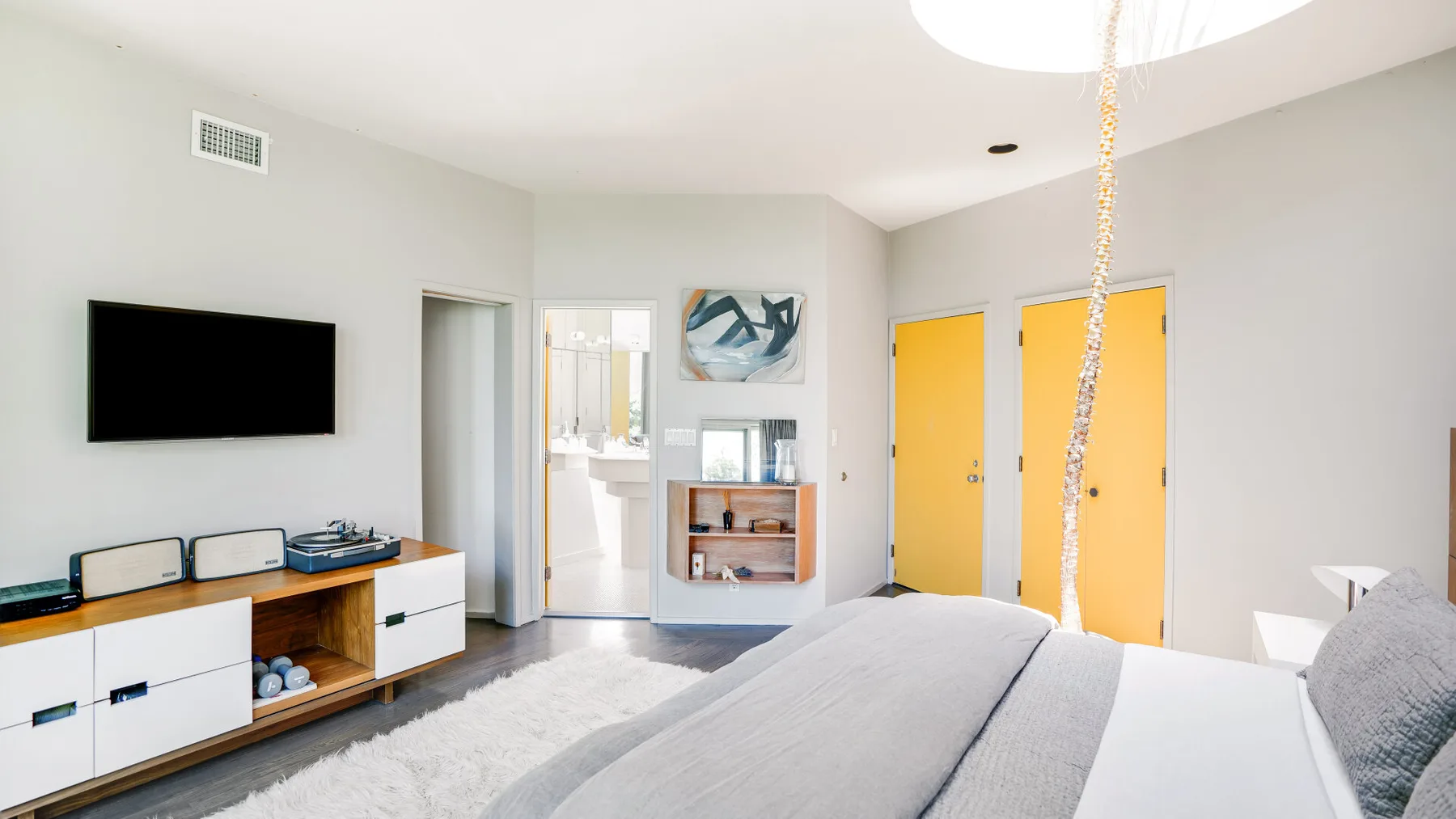A bright bedroom with a bed, wall-mounted television, and colorful doors.