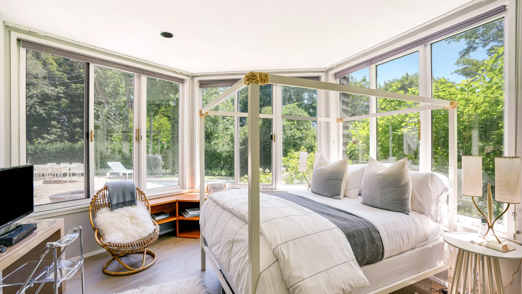 A bright bedroom with a canopy bed and large windows overlooking greenery.