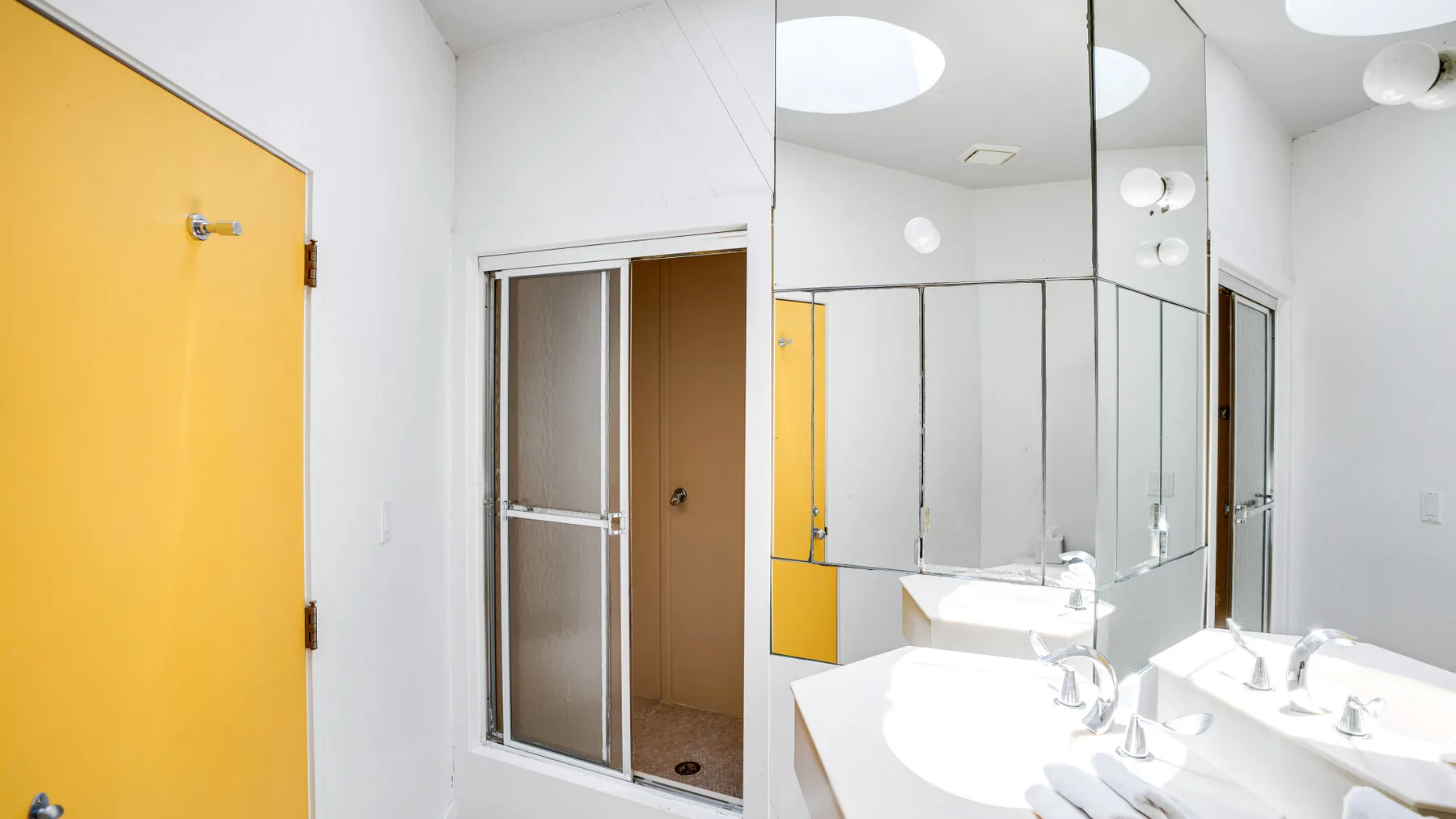 A bright bathroom with a mirrored vanity and a glass shower enclosure.